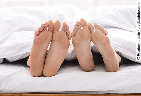 2 Fuß Paare schauen unter der Bettdecke hervor.