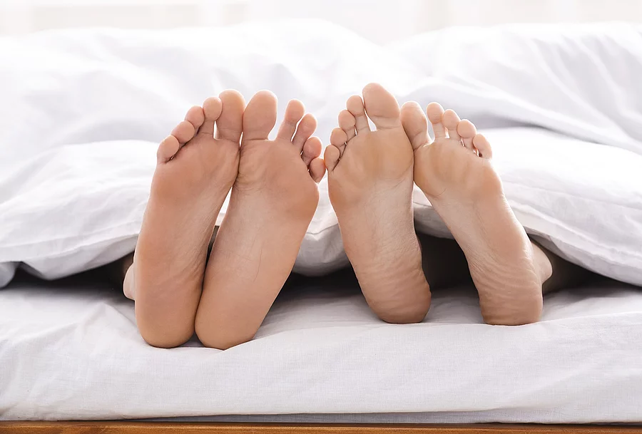 2 Fuß Paare schauen unter der Bettdecke hervor.