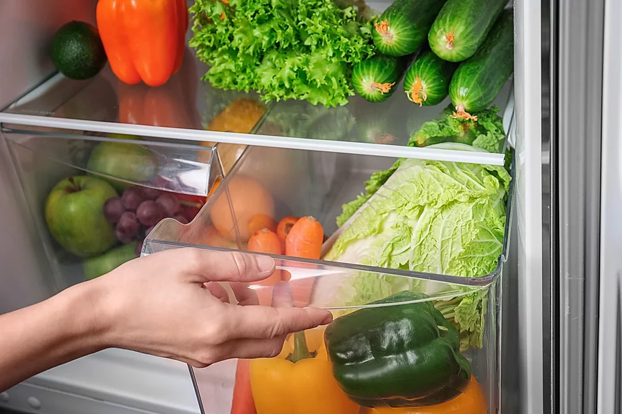 Frau öffnet ihren mit Obst und Gemüse gefüllten Kühlschrank.
