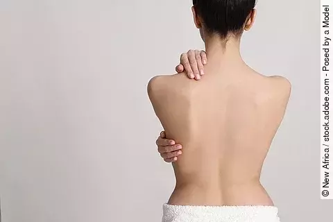 Rückenansicht einer weißen Frau, die sich den Rück hält.