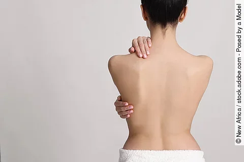 Rückenansicht einer weißen Frau, die sich den Rück hält.
