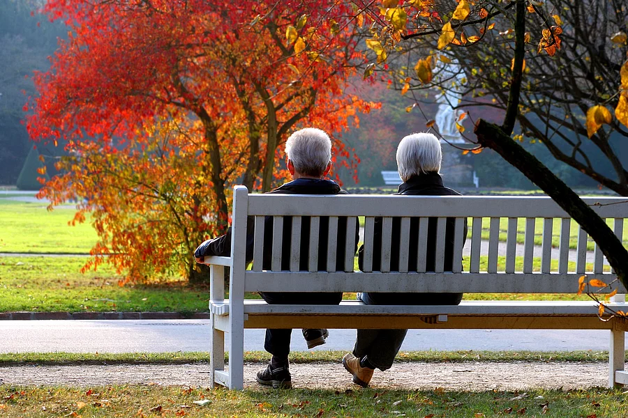 2 Senior*innen sitzen in herbstlichem Park auf einer Bank