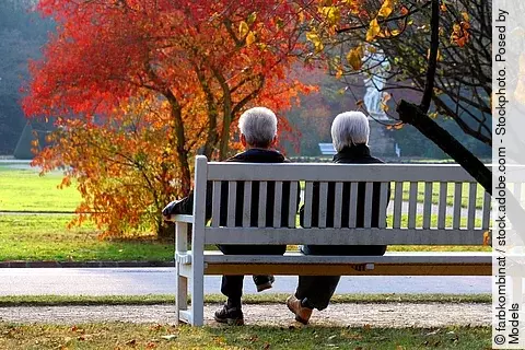 2 Senior*innen sitzen in herbstlichem Park auf einer Bank