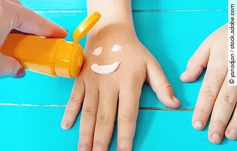 Lachender Smiley wird mit Sonnencreme auf die Hand eines Kindes gemalt.