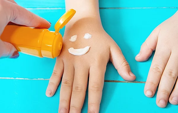 Lachender Smiley wird mit Sonnencreme auf die Hand eines Kindes gemalt.