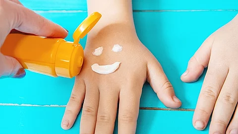 Lachender Smiley wird mit Sonnencreme auf die Hand eines Kindes gemalt.