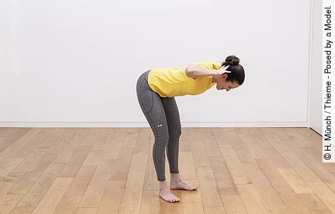 Frau steht mit leicht gebeugten Knien, Hände am Hinterkopf, Oberkörper gerade nach vorn gebeugt