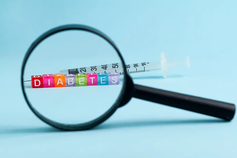 Diabetes: Lupe, dahinter Spritze vor blauem Hintergrund