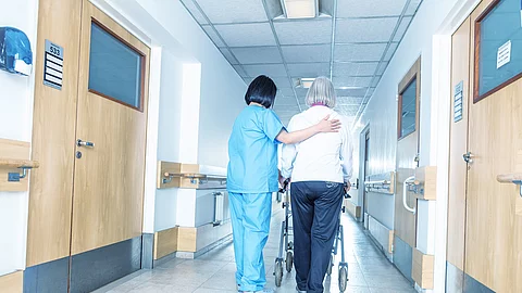Pflegerin unterstützt Patientin beim Laufen mit ihrer Gehilfe.