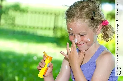 Lachendes Mädchen im Garten cremt sich das Gesicht mit Sonnencreme ein
