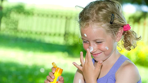 smiling girl with suncream Lachendes Mädchen im Garten cremt sich das Gesicht mit Sonnencreme ein