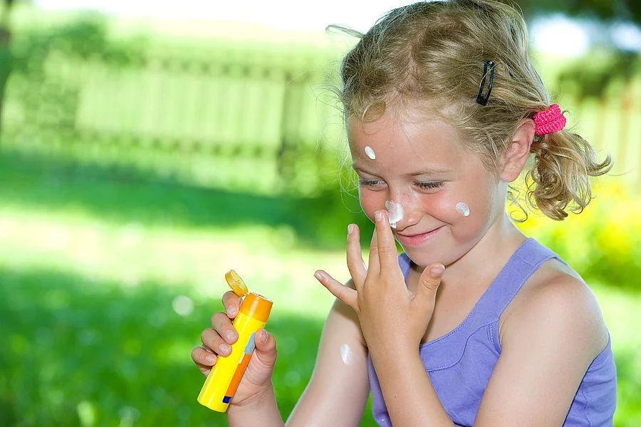 smiling girl with suncream Lachendes Mädchen im Garten cremt sich das Gesicht mit Sonnencreme ein