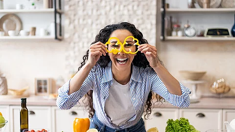 Excited woman making glasses of sweet pepper, having fun and playing with food while cooking fresh salad