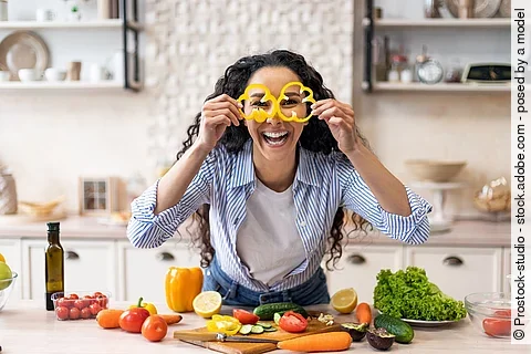 Excited woman making glasses of sweet pepper, having fun and playing with food while cooking fresh salad