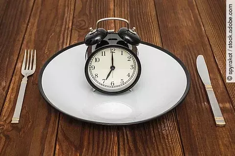 Wecker auf einem Teller, daneben Besteck