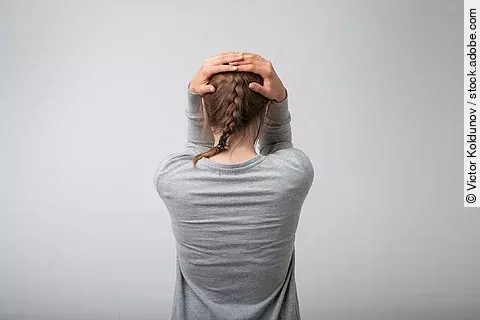 Stehende Frau von hinten, schlägt die Hände über dem Kopf zusammen