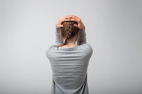 Stehende Frau von hinten, schlägt die Hände über dem Kopf zusammen