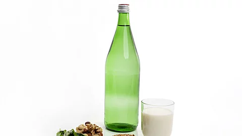 Grüne Mineralwasserflasche, Spinat, Nüsse und ein Glas Milch auf weißem Hintergrund.