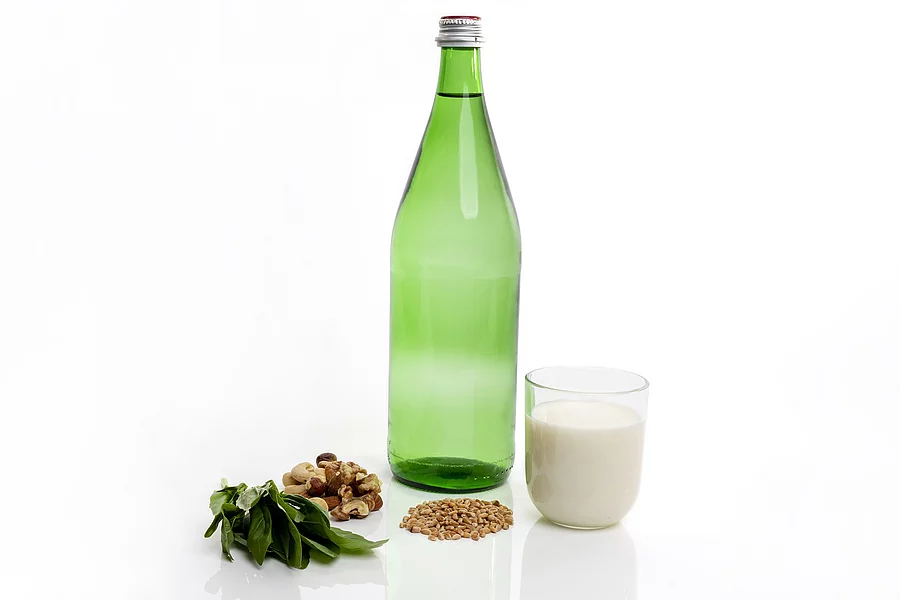 Grüne Mineralwasserflasche, Spinat, Nüsse und ein Glas Milch auf weißem Hintergrund.