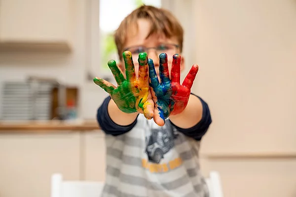 Kind mit Brille streckt die Arme nach vorne. Die Handflächen sind bunt bemalt.