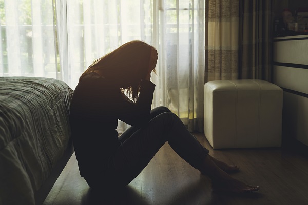 Lonely young woman feeling depressed and stressed sitting head in hands in the dark bedroom, Negative emotion and mental health concept Eine depressive Frau sitzt auf dem Boden in einem dunklen Schlafzimmer und fasst sich mit ihren Händen an den Kopf.