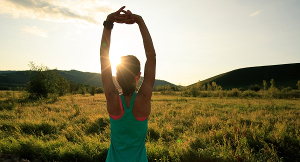 Frau dehnt sich in Sportkleidung draußen auf einem Feld.