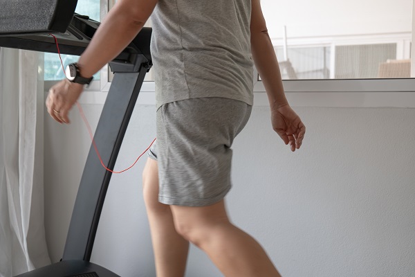 Mensch, der langsam in grauer Trainingskleidung auf dem Laufband zu Hause läuft.