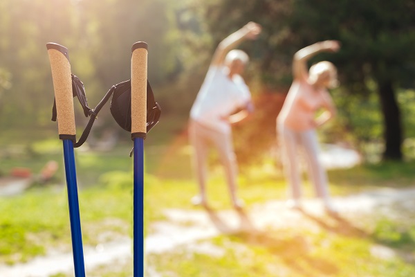 Ein älteres Ehepaar macht Sportübungen im Hintergrund (verschwommen). Im Vordergrund sind Walking Stöcke zu sehen.