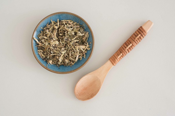 Getrocknete Heublumenblüten in einer blauen Schale und ein Holzlöffel.