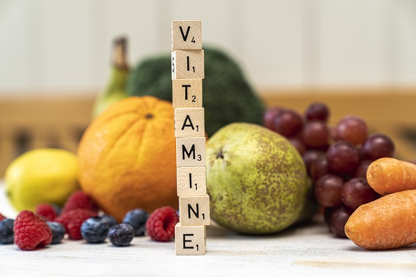 Obst und Gemüse im Hintergrund und Buchstaben auf Würfeln, die aufeinandergestapelt das Wort "Vitamine" ergeben.