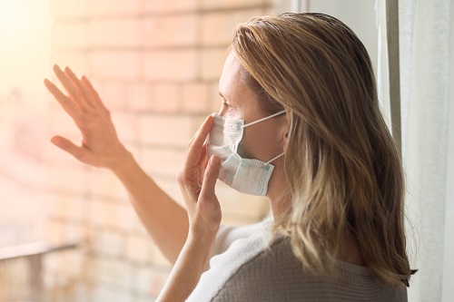 Social-Dinstancing, Frau mit Maske am Fenster